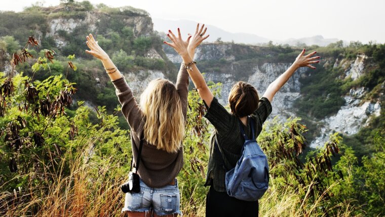 Zwei junge Frauen vor einer Natur-Kulisse mit Büschen und Bergen